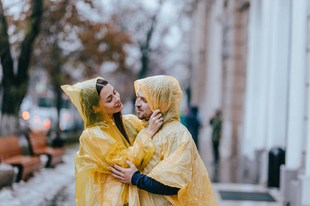 Loving couple, guy and his girlfriend dressed in yellow raincoats are hugging on the street in the rain - Φωτογραφία, εικόνα