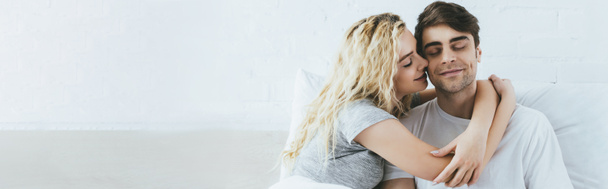 panoramic shot of attractive blonde girlfriend hugging happy boyfriend with closed eyes - Photo, Image