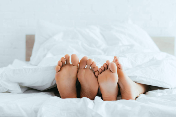 cropped view of boyfriend and girlfriend with barefoot lying in bed  - 写真・画像