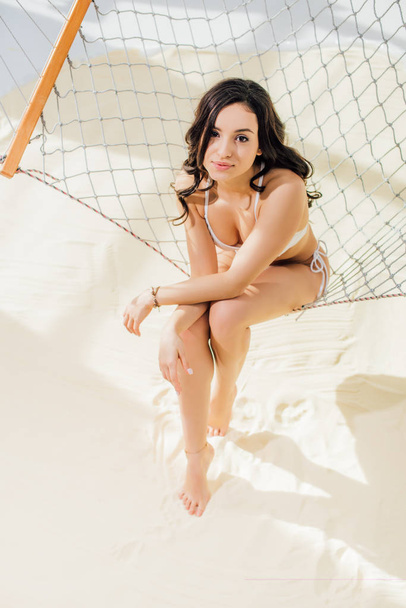beautiful girl in bikini relaxing in hammock and looking at camera on beach - Zdjęcie, obraz