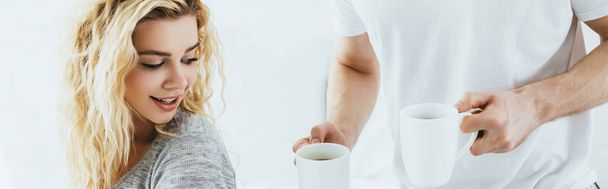 panoramic shot of man holding cups with coffee near attractive blonde woman  - Фото, зображення