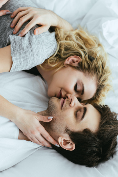 happy blonde woman kissing boyfriend while lying on bed  - Fotografie, Obrázek