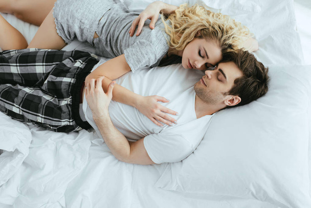 top view of happy man and woman hugging while lying on bed  - Photo, Image