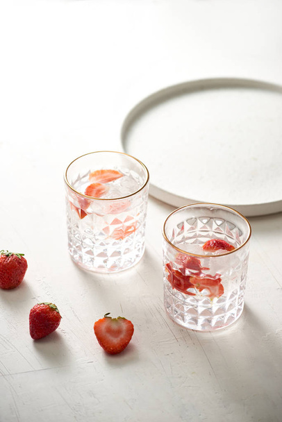 Glass of fresh, cold infused water with fresh strawberries and  fresh strawberries next to it - Foto, Imagen