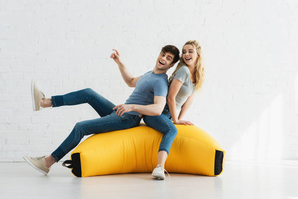 cheerful blonde girl and happy man sitting on yellow bean bag chair - Foto, afbeelding