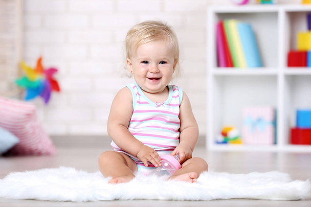 Baby girl with bottle sitting on white carpet - 写真・画像