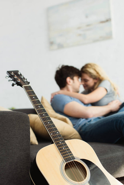 enfoque selectivo de la guitarra acústica cerca de feliz pareja abrazándose en casa
  - Foto, Imagen