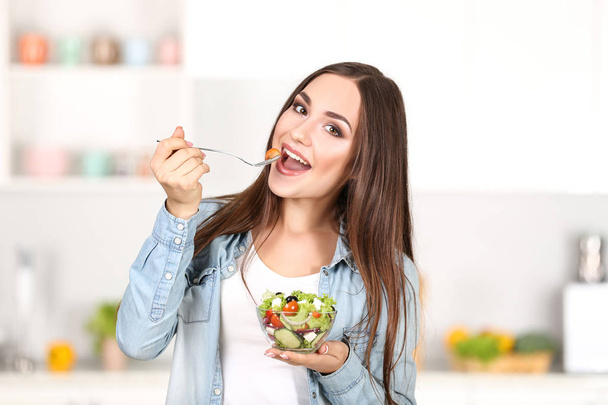 Beautiful woman eating fresh salad in the kitchen - Foto, afbeelding