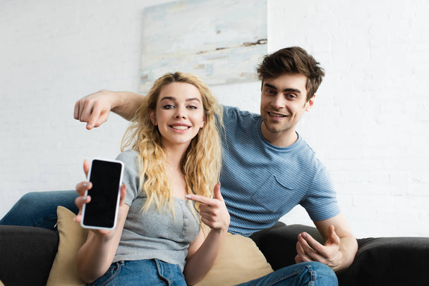 selective focus of happy man and blonde woman pointing with fingers at smartphone with blank screen - Φωτογραφία, εικόνα