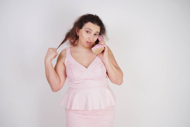emotional plump woman in pink dress talking and gossips on the Shoe like on the phone on a white Studio background - Photo, Image