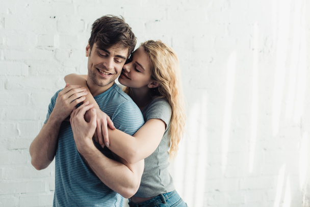 blonde cheerful girl hugging handsome and happy boyfriend  - Foto, afbeelding