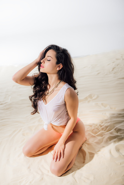 hermosa chica sexy con los ojos cerrados sentado y posando en la playa
 - Foto, Imagen