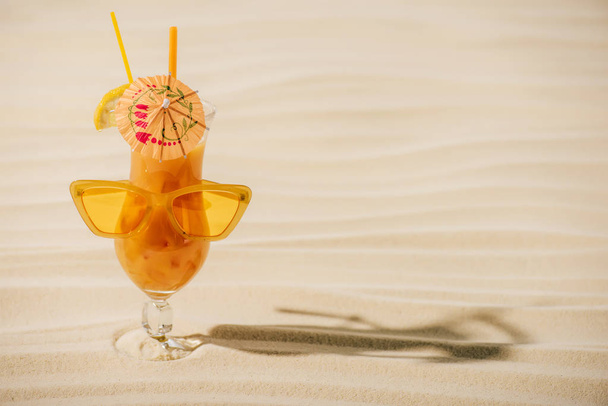 orange cocktail with sunglasses and cocktail umbrella on sandy beach with copy space - Foto, Imagen