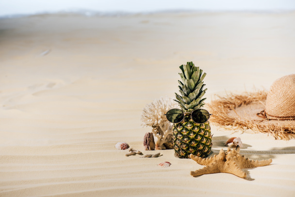 ananas avec lunettes de soleil, étoile de mer, chapeau de paille et pierres de mer sur la plage de sable avec espace de copie
 - Photo, image