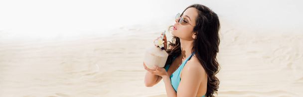 tiro panorâmico de menina em biquíni beber coquetel de coco na praia com espaço de cópia
 - Foto, Imagem