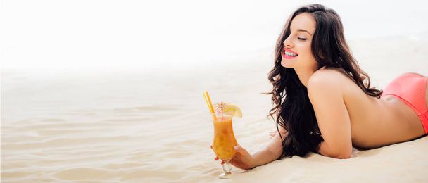 panoramic shot of smiling topless girl lying with cocktail on beach with copy space - Valokuva, kuva