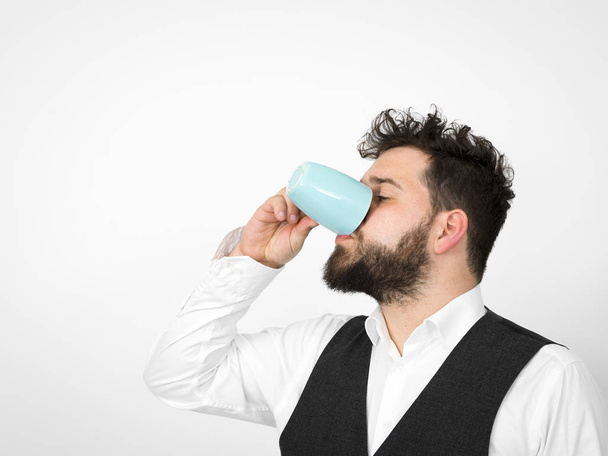 handsome man with black beard posing with turquoise coffee cup in front of white background   - Φωτογραφία, εικόνα