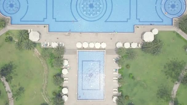 Blue swimming pool, umbrellas and green lawn in luxury resort hotel aerial view. Large swimming pool in hotel and sandy sea beach view from above flying drone. - Záběry, video