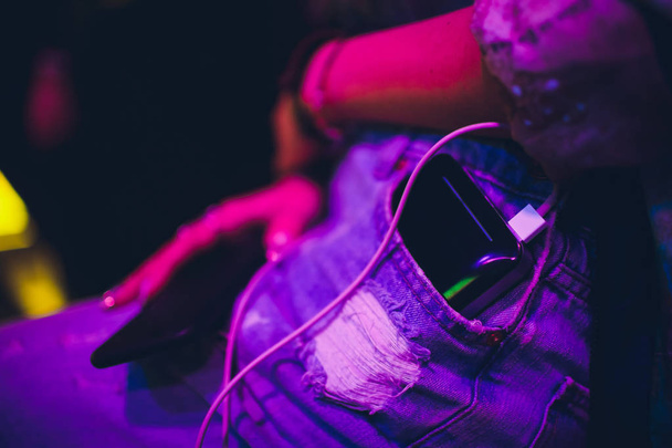 Black power bank lies in front pocket of blue jeans and is charging a mobile phone. Keep the battery charged on your device anyway you go. Technology connect with white cord close up. - Photo, image