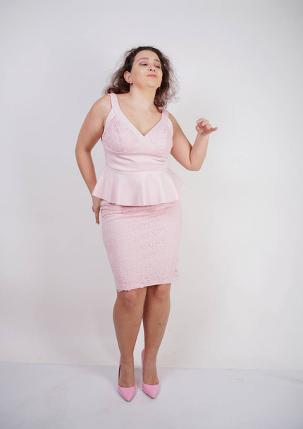 pretty chubby positive girl dancing in pink fashionable dress on white studio background - Foto, imagen