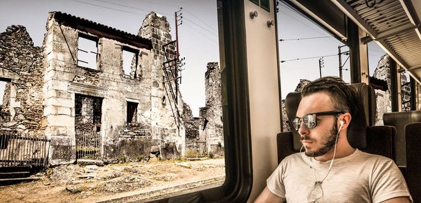 νεαρός άνδρας που βλέπει την πόλη να καταστρέφεται μέσα από το παράθυρο του τρένου - Φωτογραφία, εικόνα
