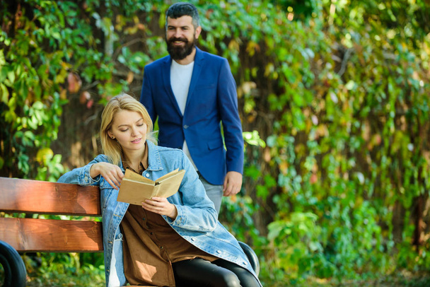 Man came to girlfriend on date. Girl sit bench read book while wait boyfriend. Romantic relations concept. Romantic date. Couple in love romantic date nature park background. Surprise for her - 写真・画像