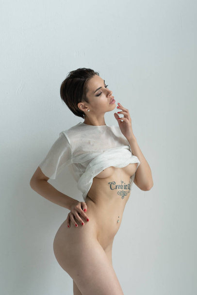 молодая красивая девушка с татуировкой, позирующая обнаженной в студии, стоящая в белом белье
 - Фото, изображение