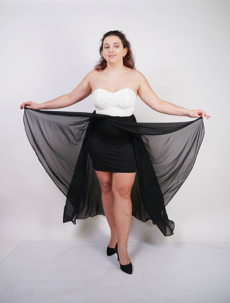 charming chubby happy woman standing in flying evening dress on white studio background alone - Foto, afbeelding