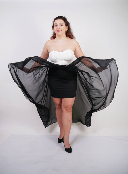 charming chubby happy woman standing in flying evening dress on white studio background alone - Фото, зображення