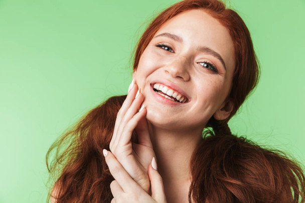 Beautiful happy young redhead girl posing isolated over green wall background. - 写真・画像