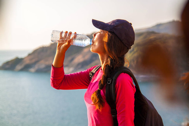一人の女性バックパッカーは、水の飲み物のために停止し、山の頂上からの眺めを楽しんでいます . - 写真・画像