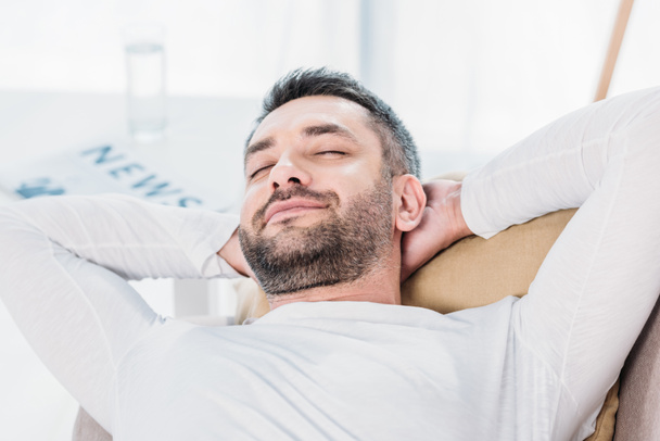 селективное внимание красивого бородатого мужчины с закрытыми глазами и руками за спиной, лежащими на диване дома
 - Фото, изображение