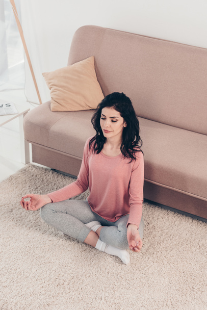 Hochwinkelaufnahme der schönen Frau in Lotus-Pose praktiziert Meditation zu Hause im Wohnzimmer - Foto, Bild