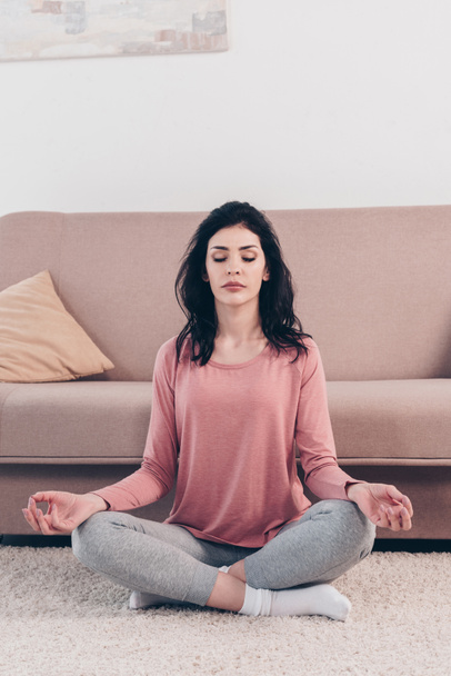 bela mulher com os olhos fechados em Lotus Pose praticando meditação na sala de estar em casa
  - Foto, Imagem