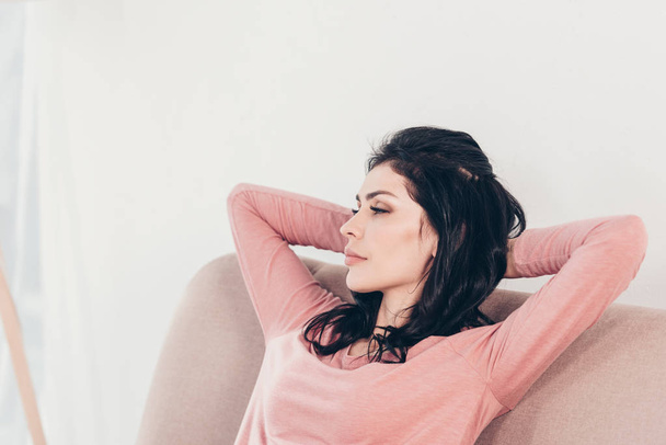 beautiful woman resting on couch with hands behind head at home - Photo, image