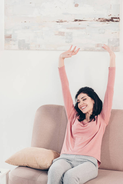krásná usměvavá žena sedící na pohovce s napřaženou rukou doma - Fotografie, Obrázek