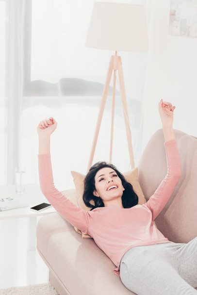 beautiful smiling woman with Raised Hands resting on couch at home - Foto, Bild