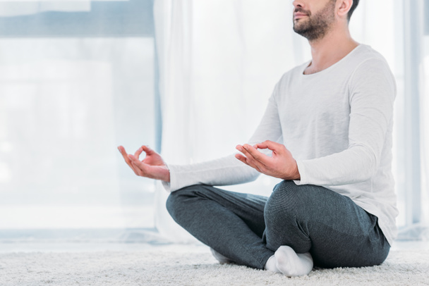 обрезанный вид человека, сидящего на ковре в Lotus Pose и медитирующего дома
 - Фото, изображение