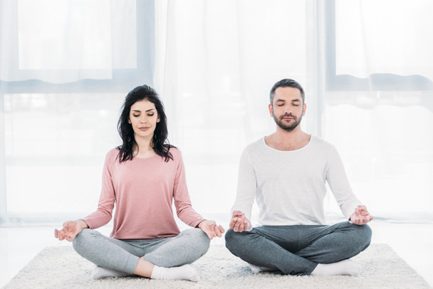 Frau und Mann mit geschlossenen Augen sitzen in Lotuspose und meditieren zu Hause - Foto, Bild