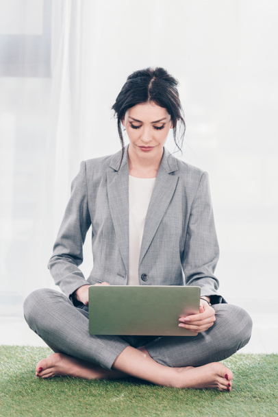 beautiful businesswoman in suit sitting on grass mat and using laptop - Photo, Image