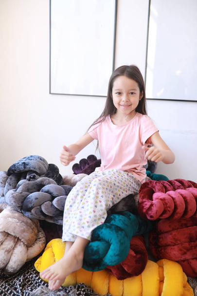 Child girl plays among unusual pillows in pajamas. - Foto, Imagem