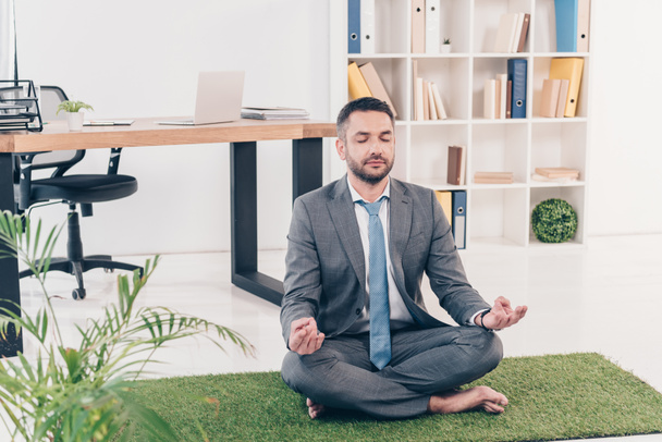 obchodník, který sedí na travních rohoži v Lotus Pose a medituje v úřadu - Fotografie, Obrázek