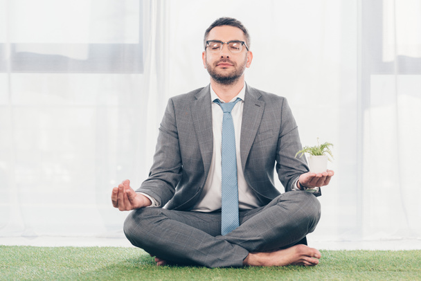 businessman in glasses on grass mat meditating while sitting in Lotus Pose  - Foto, imagen