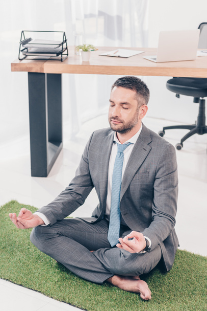zittend op gras mat in Lotus pose en mediteren in Office - Foto, afbeelding