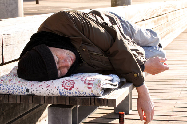 Бездомный или беженец спит на деревянной скамейке
  - Фото, изображение