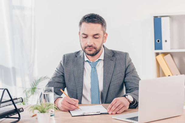 hombre de negocios guapo en traje sentado en el escritorio y la escritura en la oficina
 - Foto, imagen
