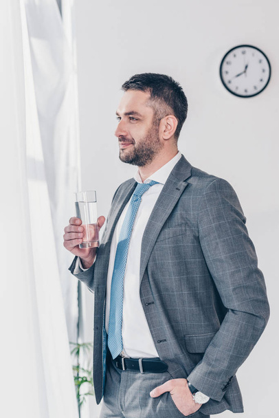 handsome businessman in suit holding glass of water in office - Φωτογραφία, εικόνα