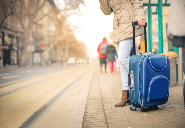 Chica joven con maleta azul esperando tranvía
 - Foto, Imagen