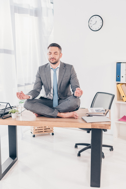 オフィスデスクに座っている間、ロータスポーズで瞑想スーツのハンサムなビジネスマン - 写真・画像