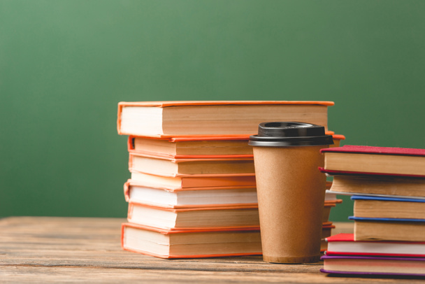Books and disposable cup on wooden surface on green - Foto, Bild